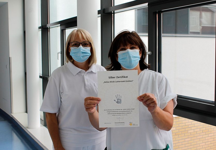 Steffi John und Katharina Blessin (v.l.n.r.), Fachschwestern für Krankenhaushygiene, präsentieren das Silber-Zertifikat der „Aktion Saubere Hände“. (Foto: Helios Kliniken Mansfeld-Südharz)