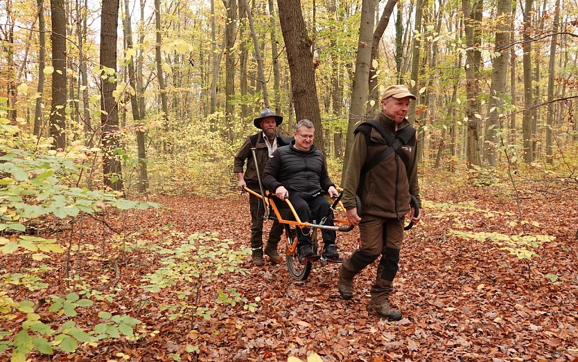 Auf dem Wanderrollstuhl Joelette l&auml;sst sich auch im Herbst auf feuchten und rutschigeren Wegen der Wald vortrefflich erleben. Das best&auml;tigen der Inklusionsbotschafter Marco Pompe (Mitte) sowie die Ranger Christian Sch&ouml;pke (links) und Christian Volk. (Foto: Lisa M&auml;der)