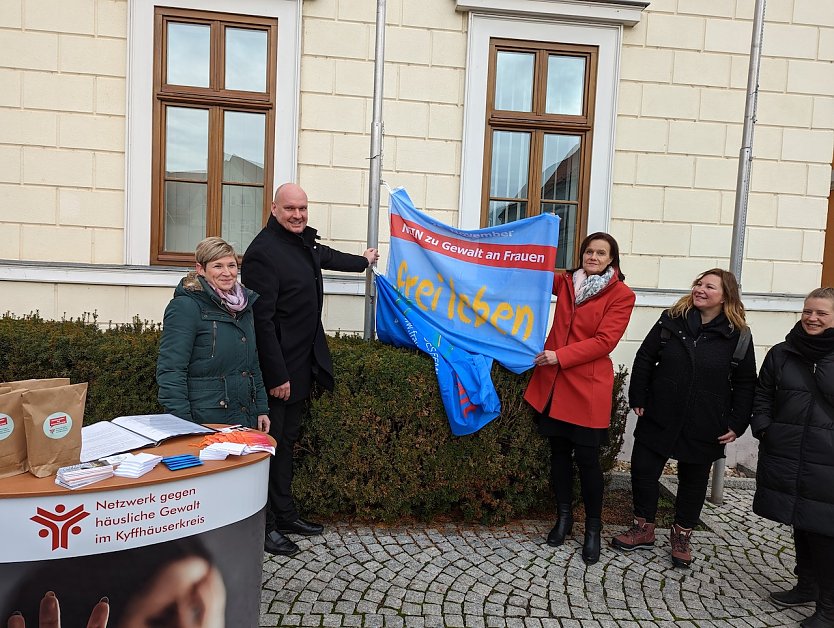 andr&auml;tin Antje Hochwind-Schneider (3.v.re.) und B&uuml;rgermeister Steffen Grimm (2.v.li.) hissen beim Aktionstag gegen h&auml;usliche Gewalt die Flagge als Symbol f&uuml;r die gemeinsame Zusammenarbeit gegen Gewalt an Frauen und M&auml;dchen im Kyffh&auml;userkreis. (Foto: Janne Skara)